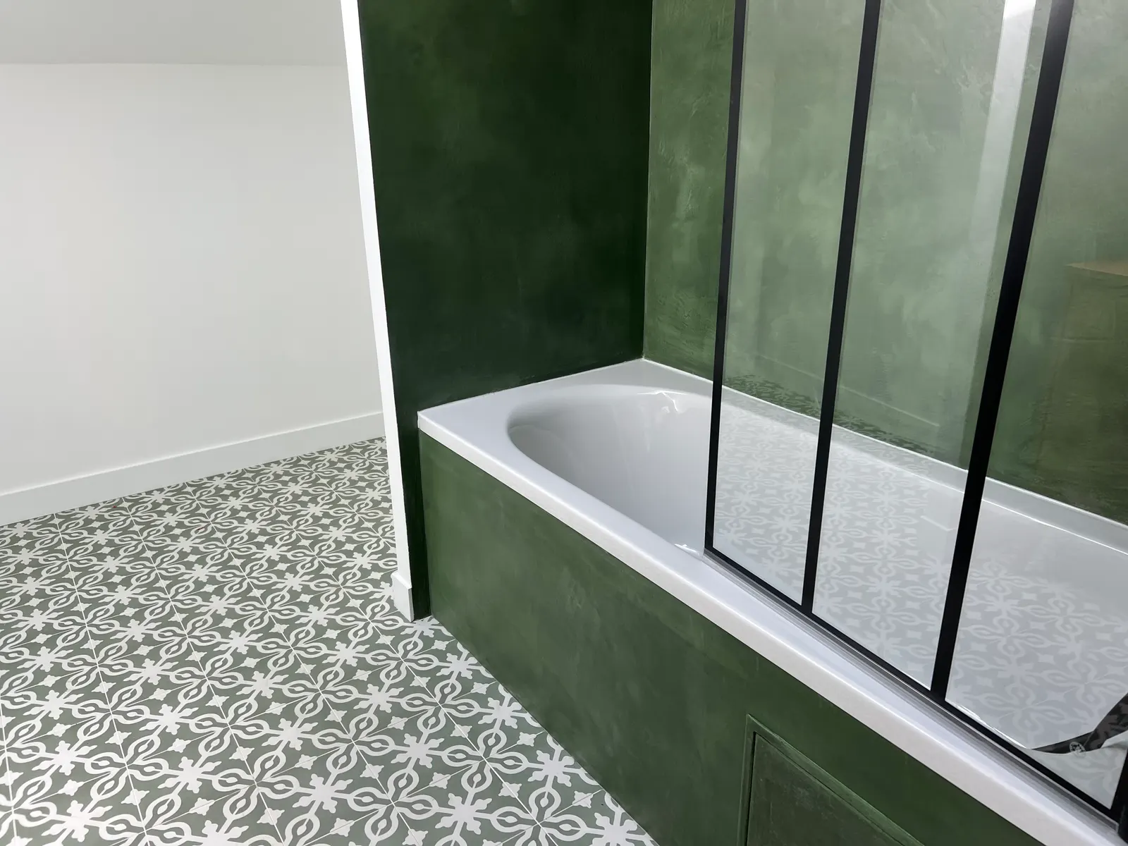 Baignoire habillée de béton ciré vert profond, avec murs assortis et pare-baignoire verrière noir